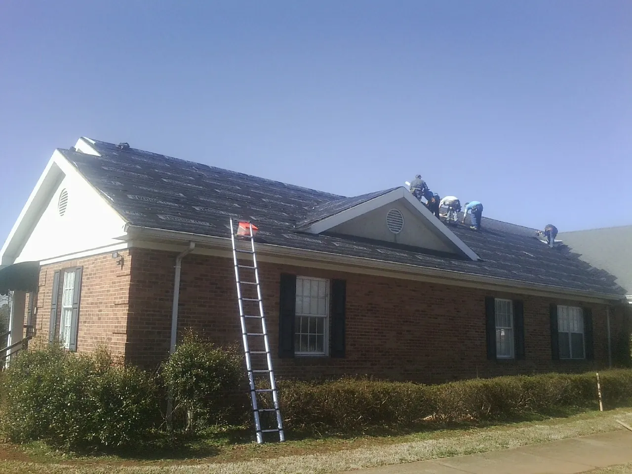 Crew tearing shingles off a brick ranch roof with a ladder set — Emergency Roof Repair work by our crew in Valparaiso