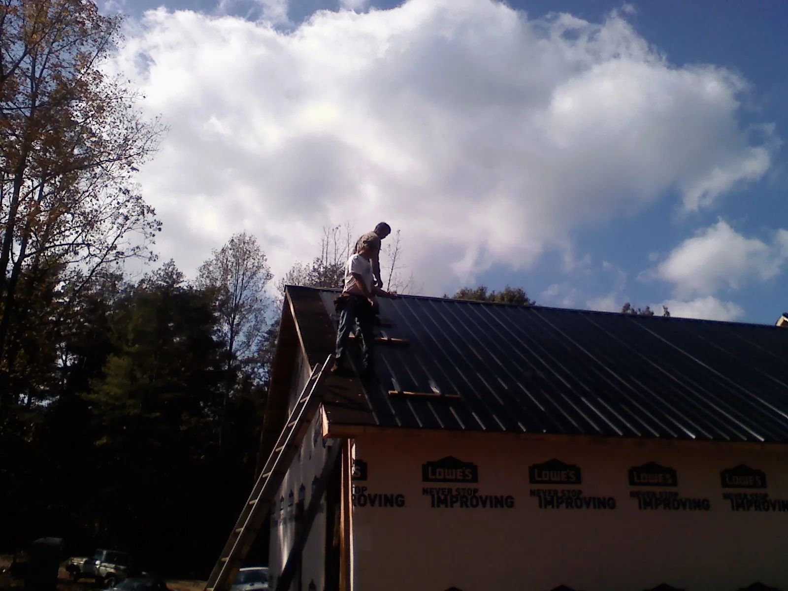 Roofer fastening dark metal panels high against a cloudy sky, from a Roof Inspection job in Valparaiso