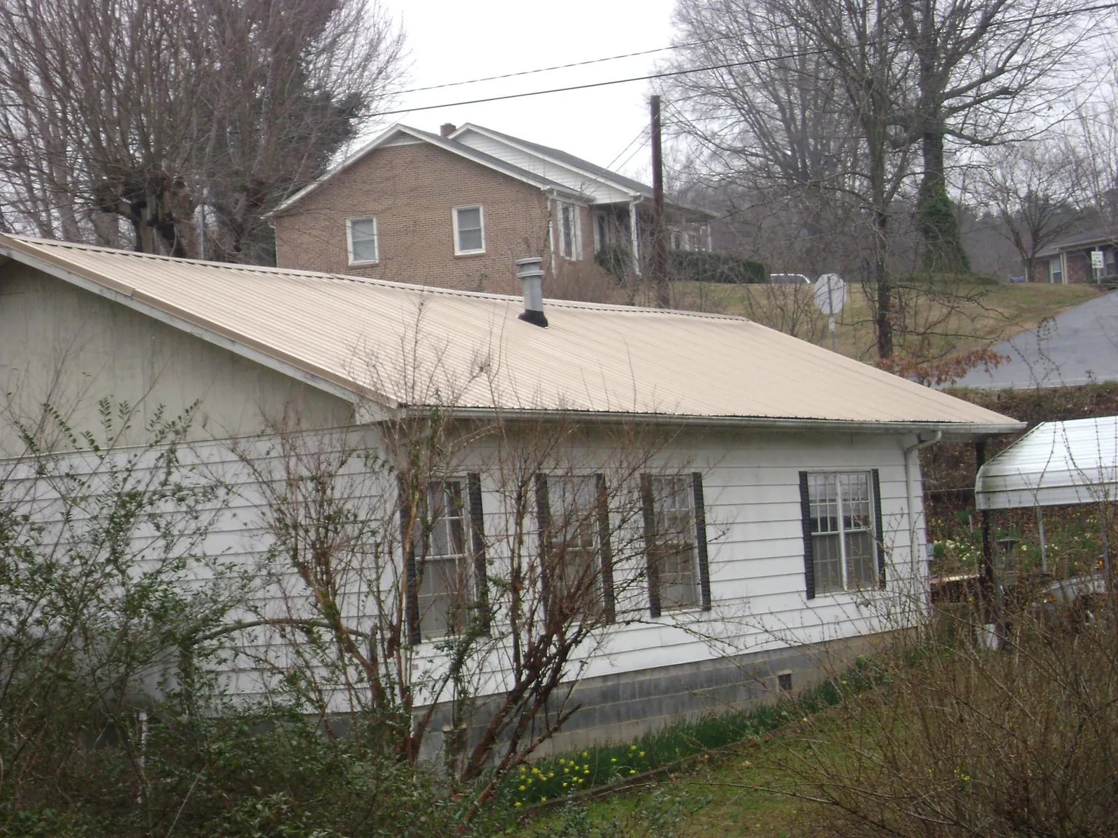 Tan metal roof on a white sided house set into a hillside — Commercial Roofing by Roofing Brothers in Valparaiso